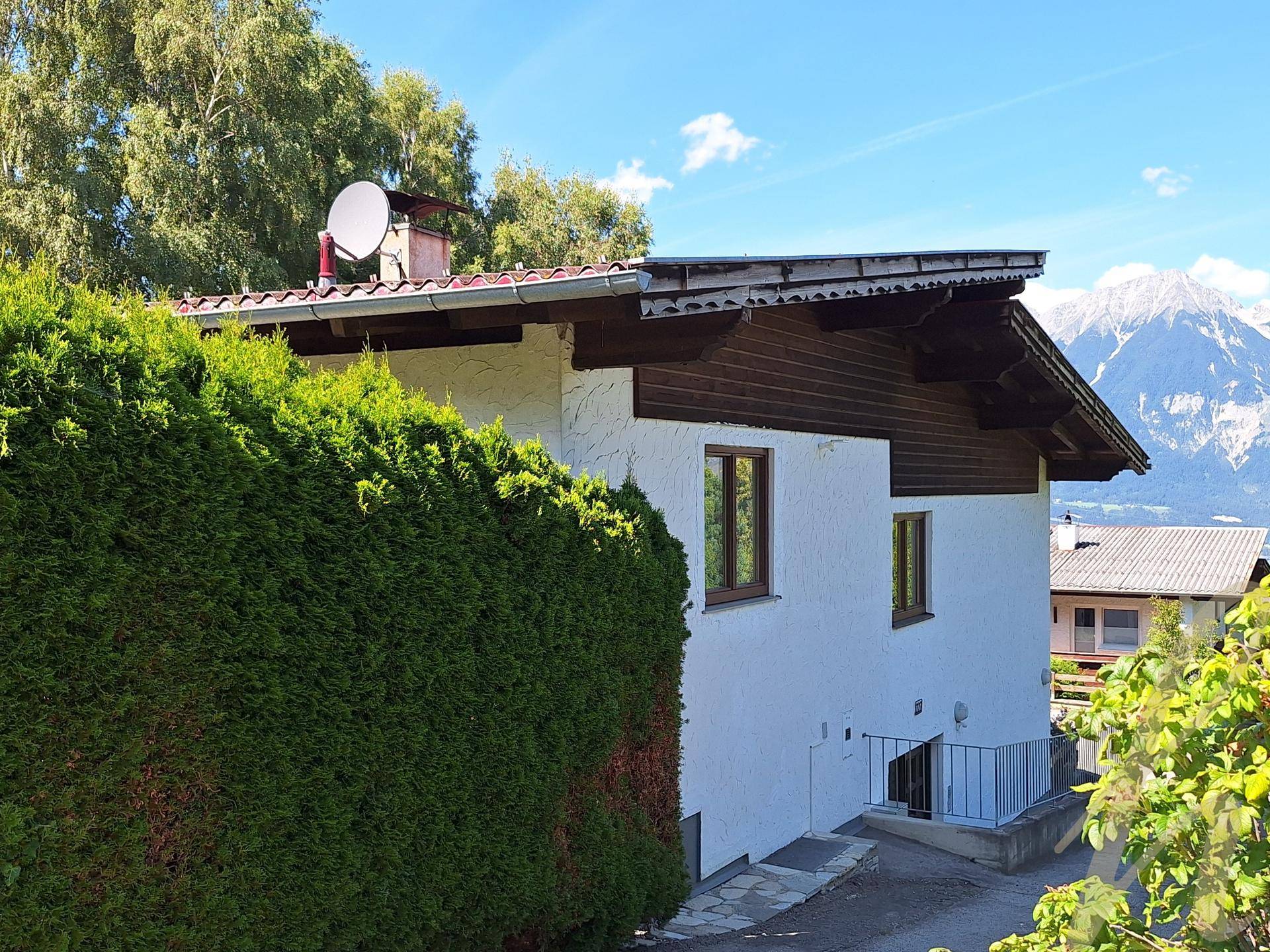 Seitenansicht des Hauses mit Satteldach, Satellitenschüssel und Blick auf die Berge in der Ferne.