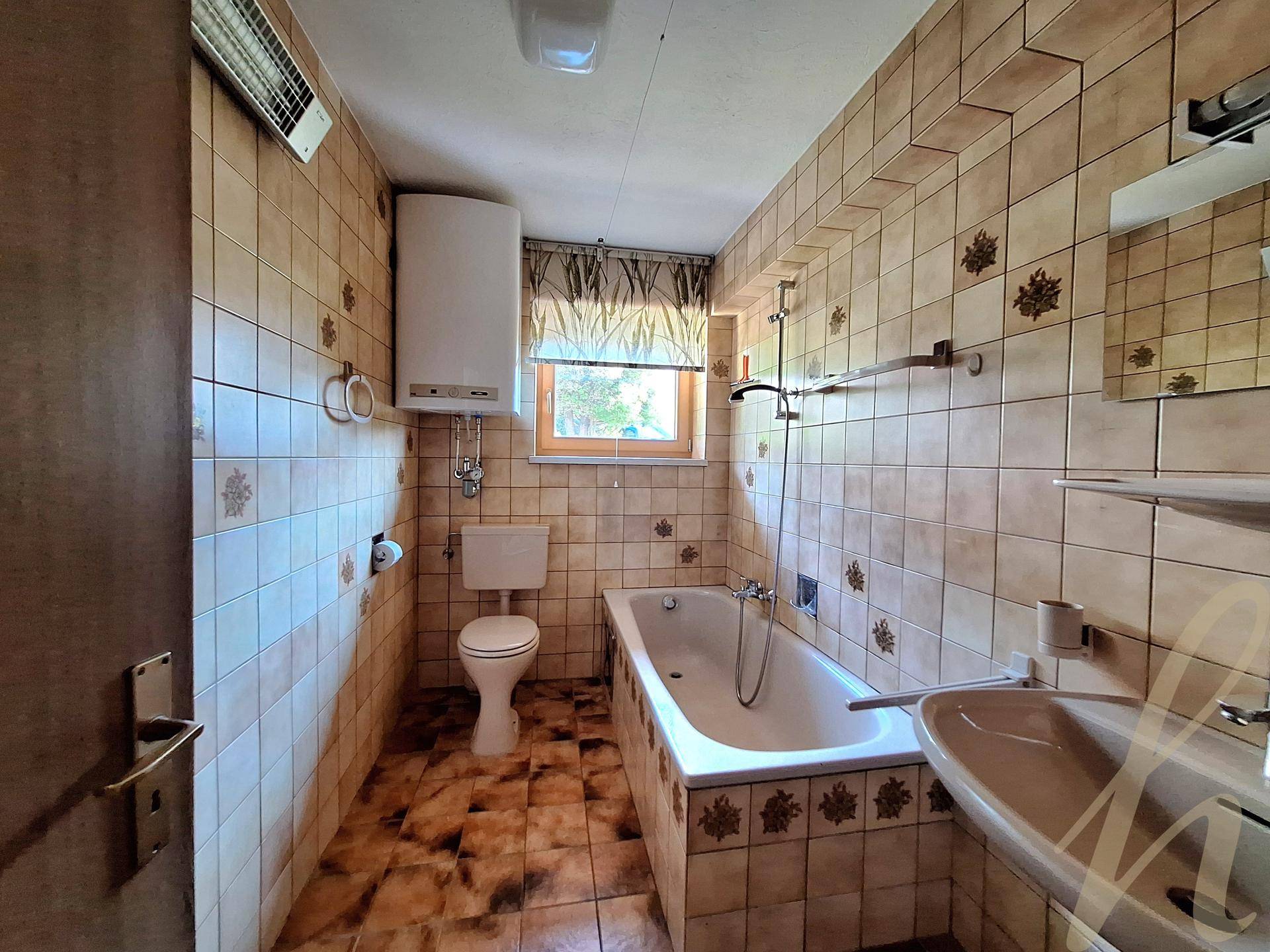 Badezimmer im 80er-Jahre-Stil mit Badewanne, WC, Waschbecken und gemusterten Fliesen.