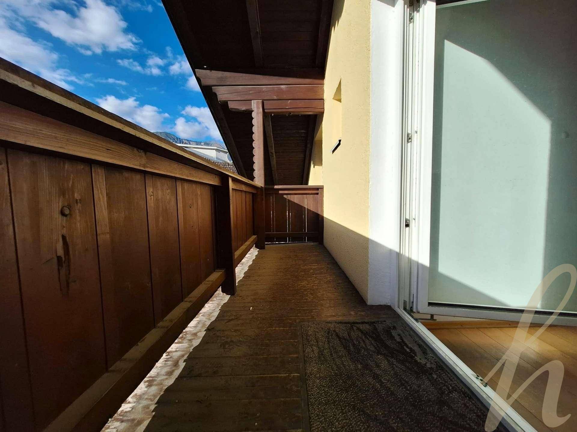 Langer Balkon mit Holzverkleidung und Zugang zum Innenbereich durch eine Glastür.