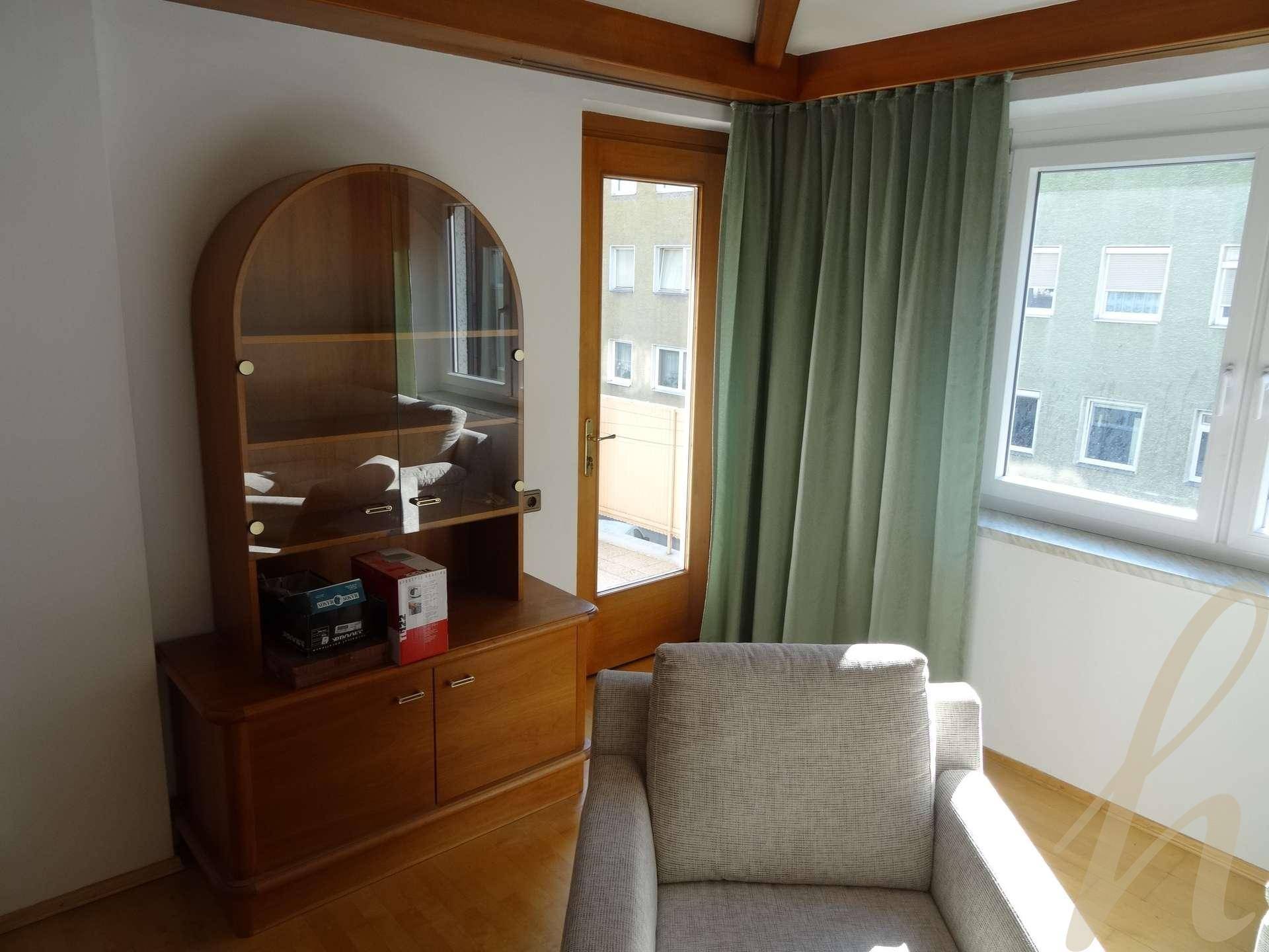 Innenraum mit Holzschrank, Sessel und Zugang zu einem Außenbereich durch eine Glastür.