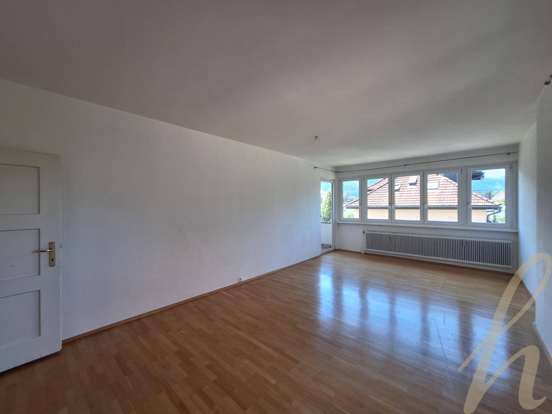 Geräumiges Wohnzimmer mit Parkettboden, großen Fenstern und viel Tageslicht.