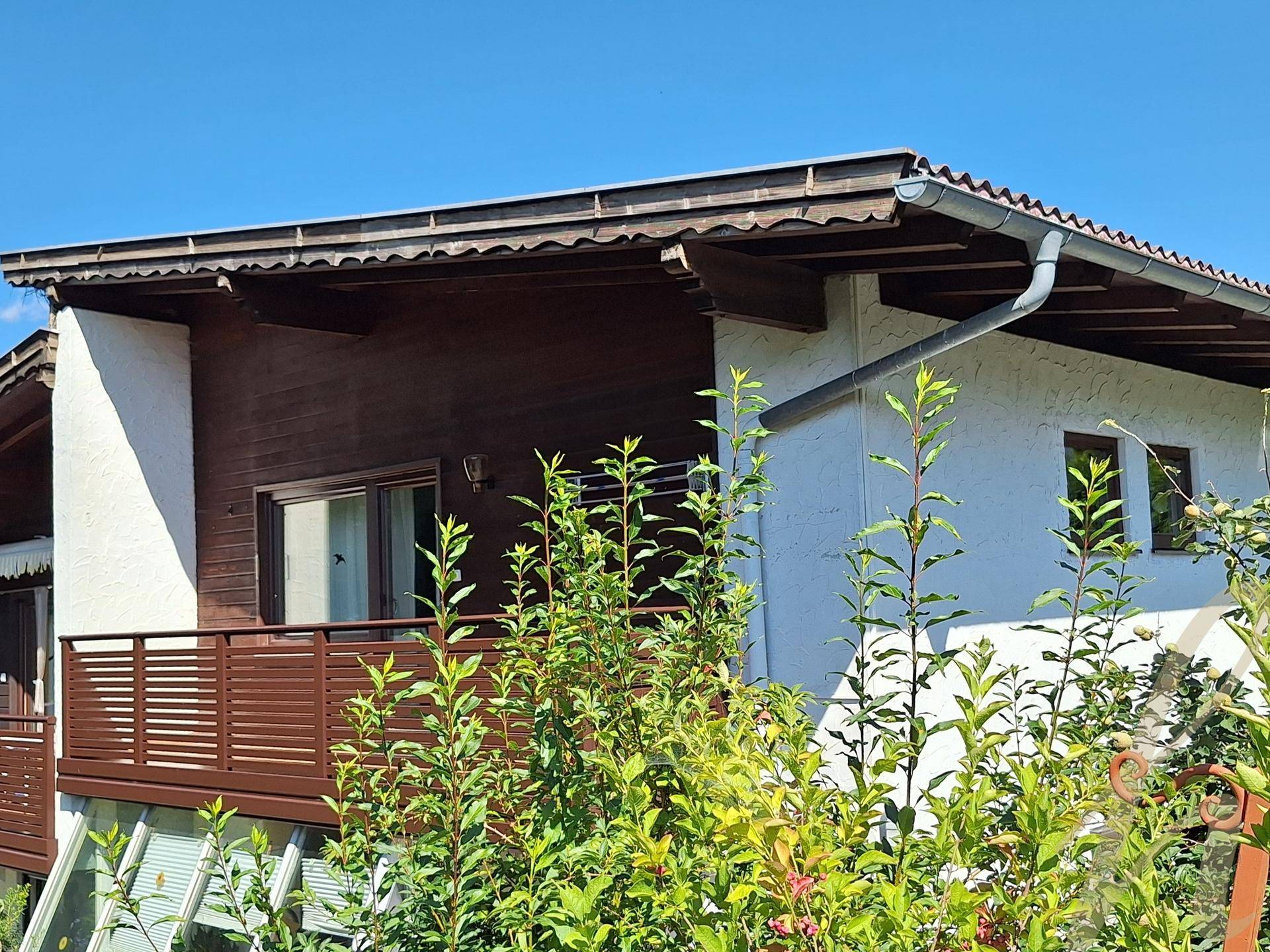 Seitenansicht des Hauses mit Balkon und Holzelementen, umgeben von grünen Pflanzen.
