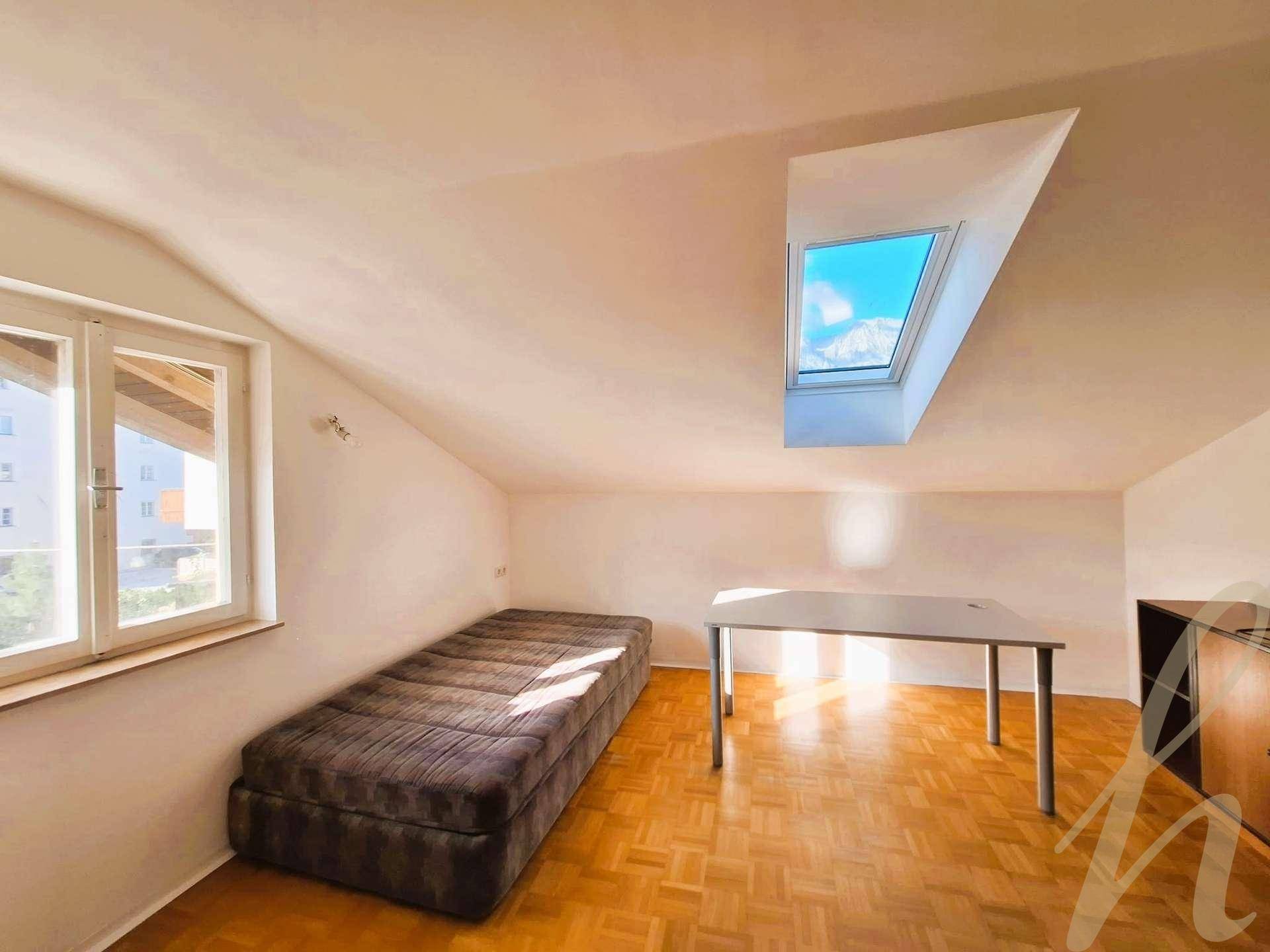 Heller Dachbodenraum mit Holzboden, Einzelbett und Dachfenster mit Bergblick.