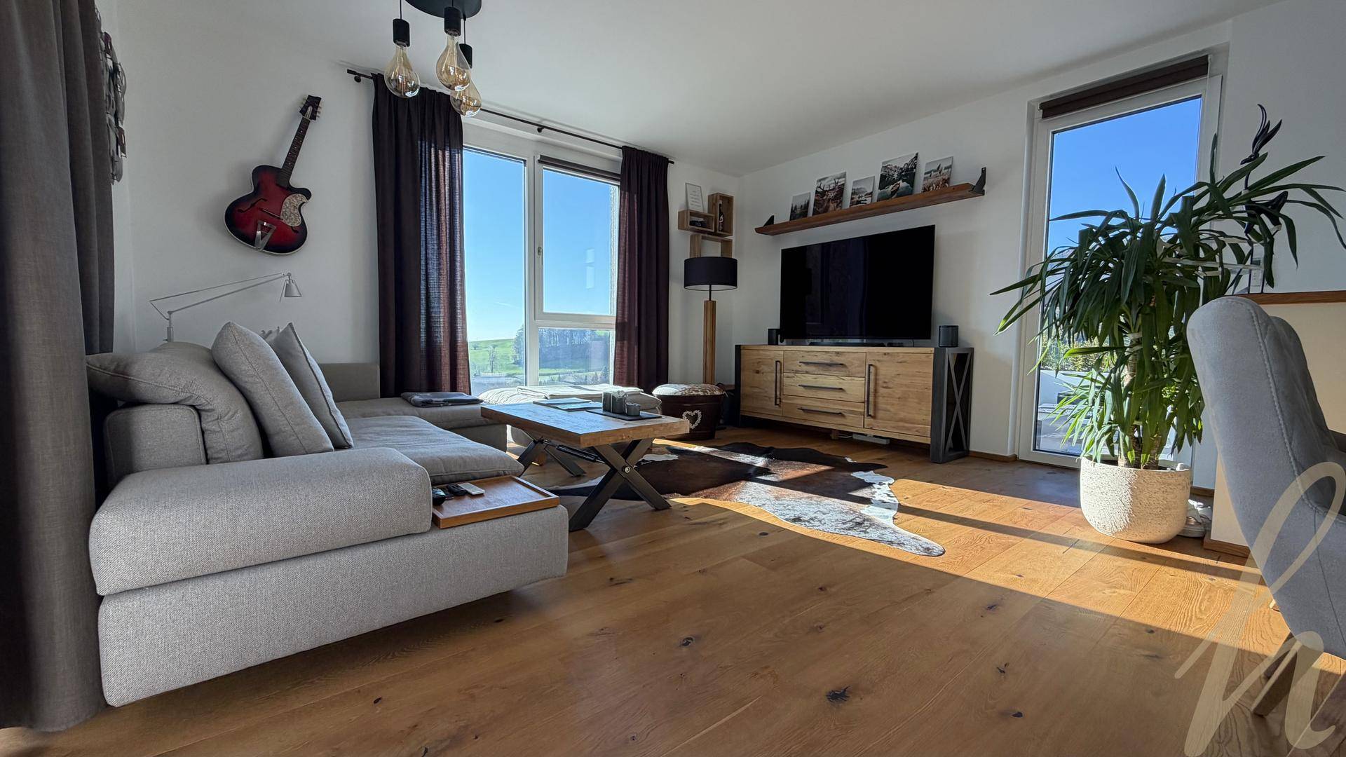 Helles Wohnzimmer mit bequemer Couch, Holzboden und großen Fenstern für viel Tageslicht.