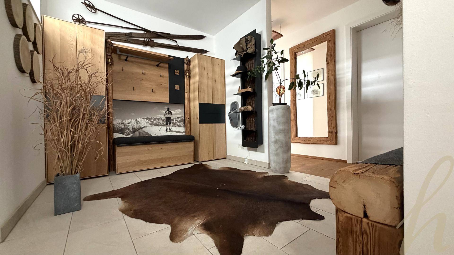 Gemütlicher Flur mit Holzelementen, einer Sitzbank und einem Kuhfellteppich im alpinen Stil.