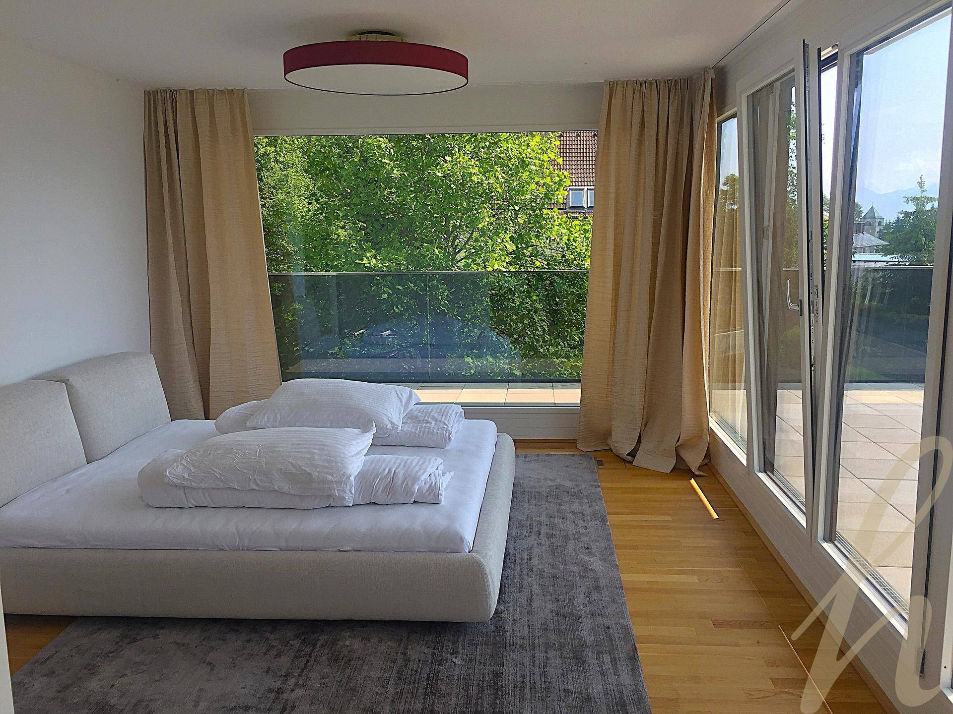 Helles Schlafzimmer mit Zugang zur Terrasse, umgeben von grünen Bäumen und viel natürlichem Licht.