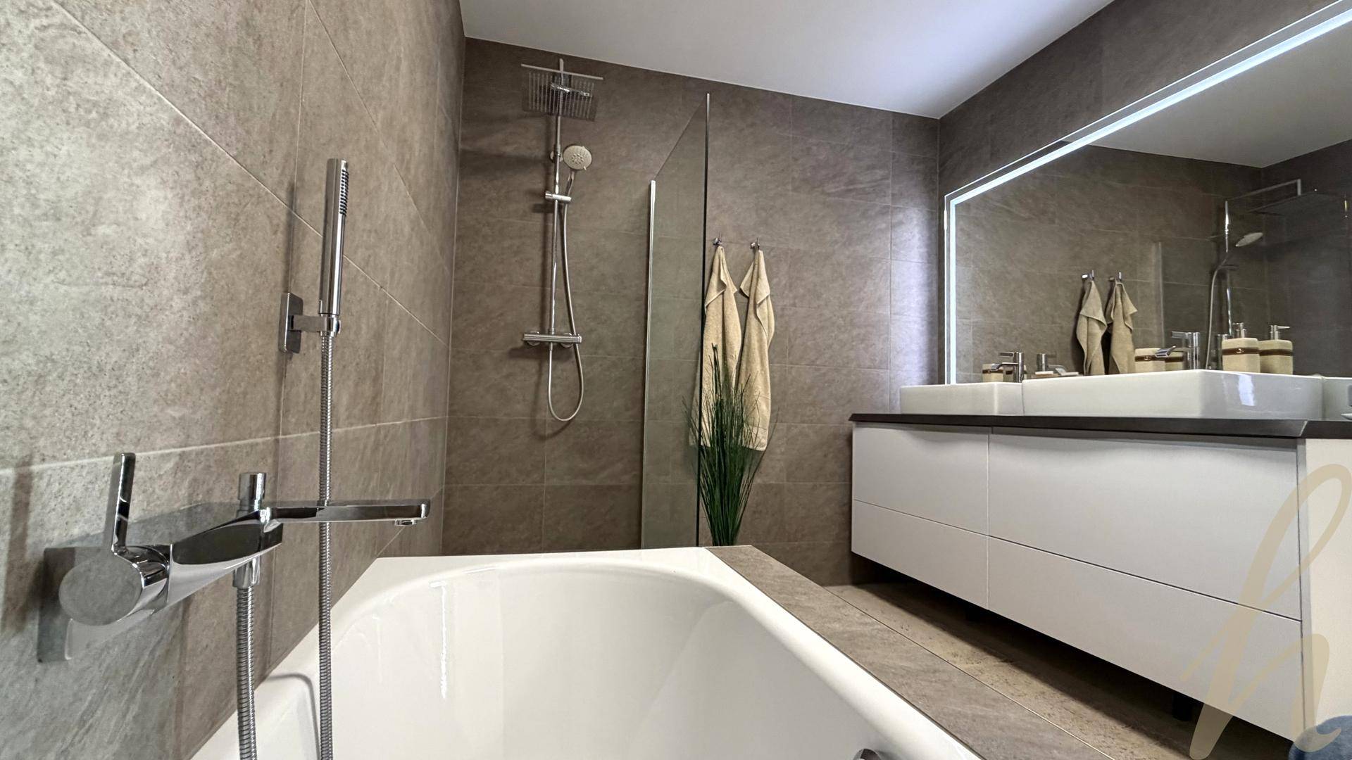 Stilvolles Badezimmer mit Badewanne, Duschbereich und großem Waschtisch mit Spiegel.