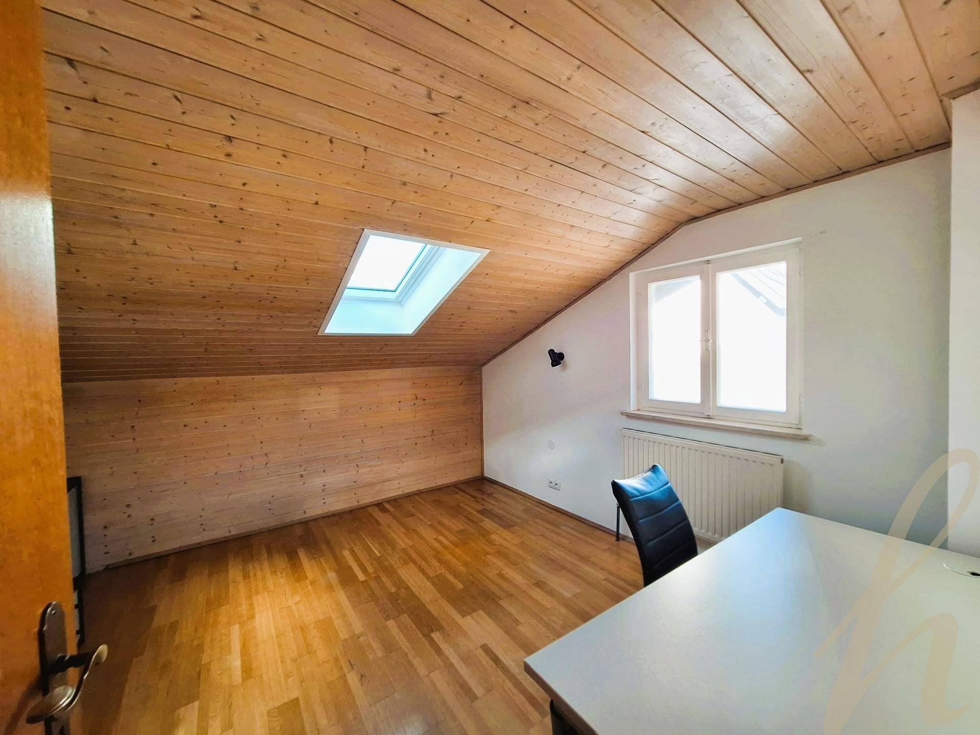 Heller Dachbodenraum mit Holzdecke, Holzboden, Dachfenster und Arbeitsbereich.