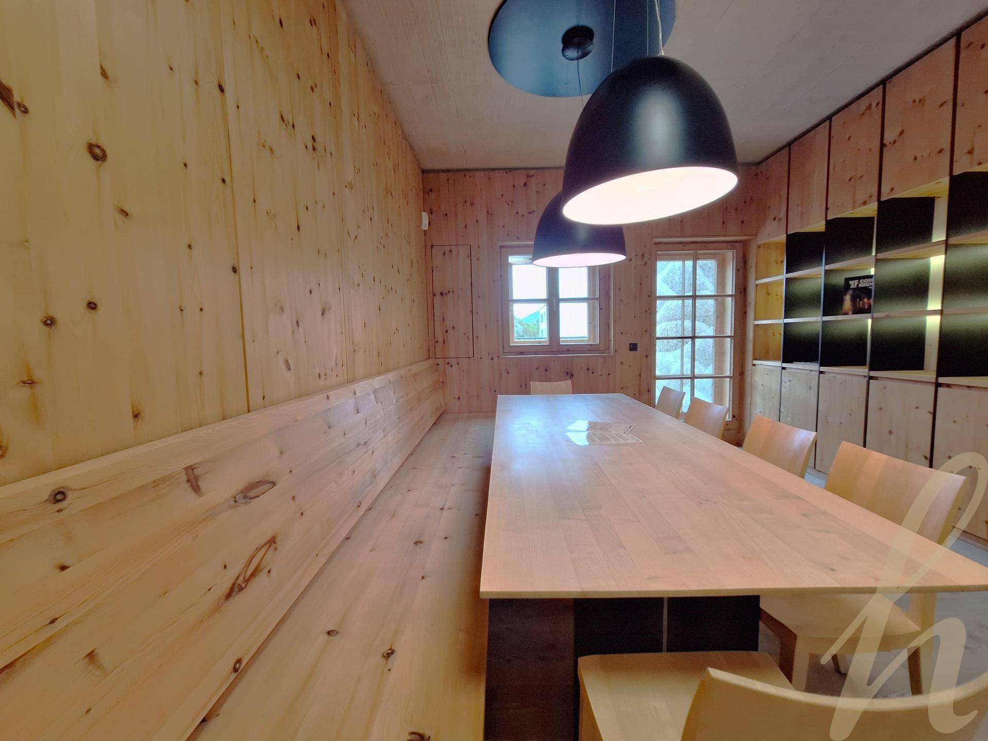 Rustikaler Essbereich mit Holztäfelung, langer Holztafel und passenden Bänken, beleuchtet von modernen Pendelleuchten.