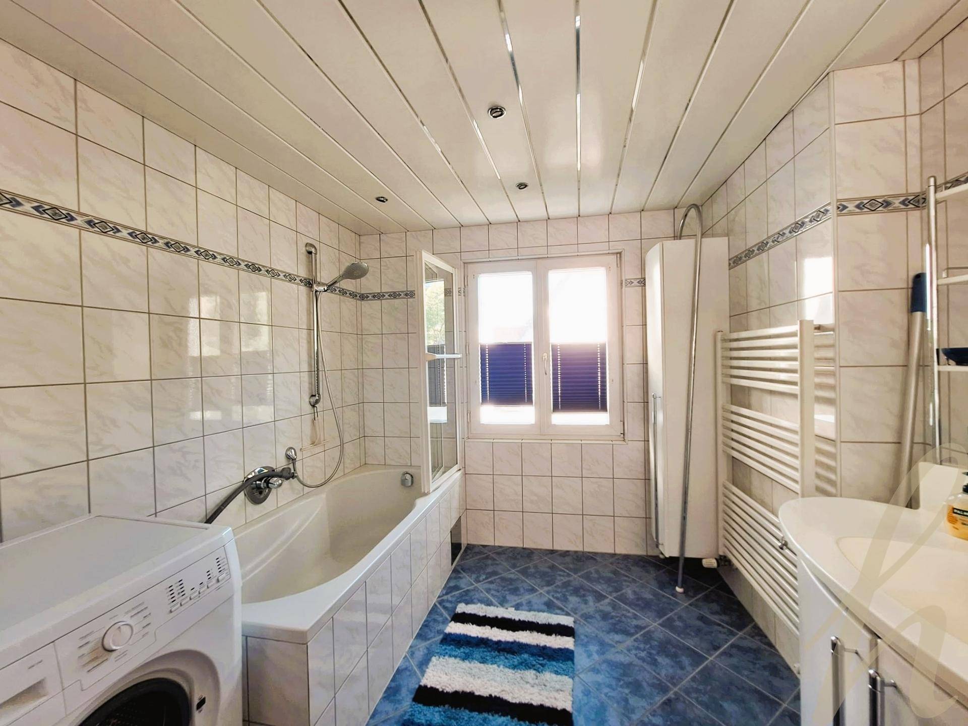 Badezimmer mit weißen Wandfliesen, blauen Bodenfliesen, Badewanne und Waschmaschine.