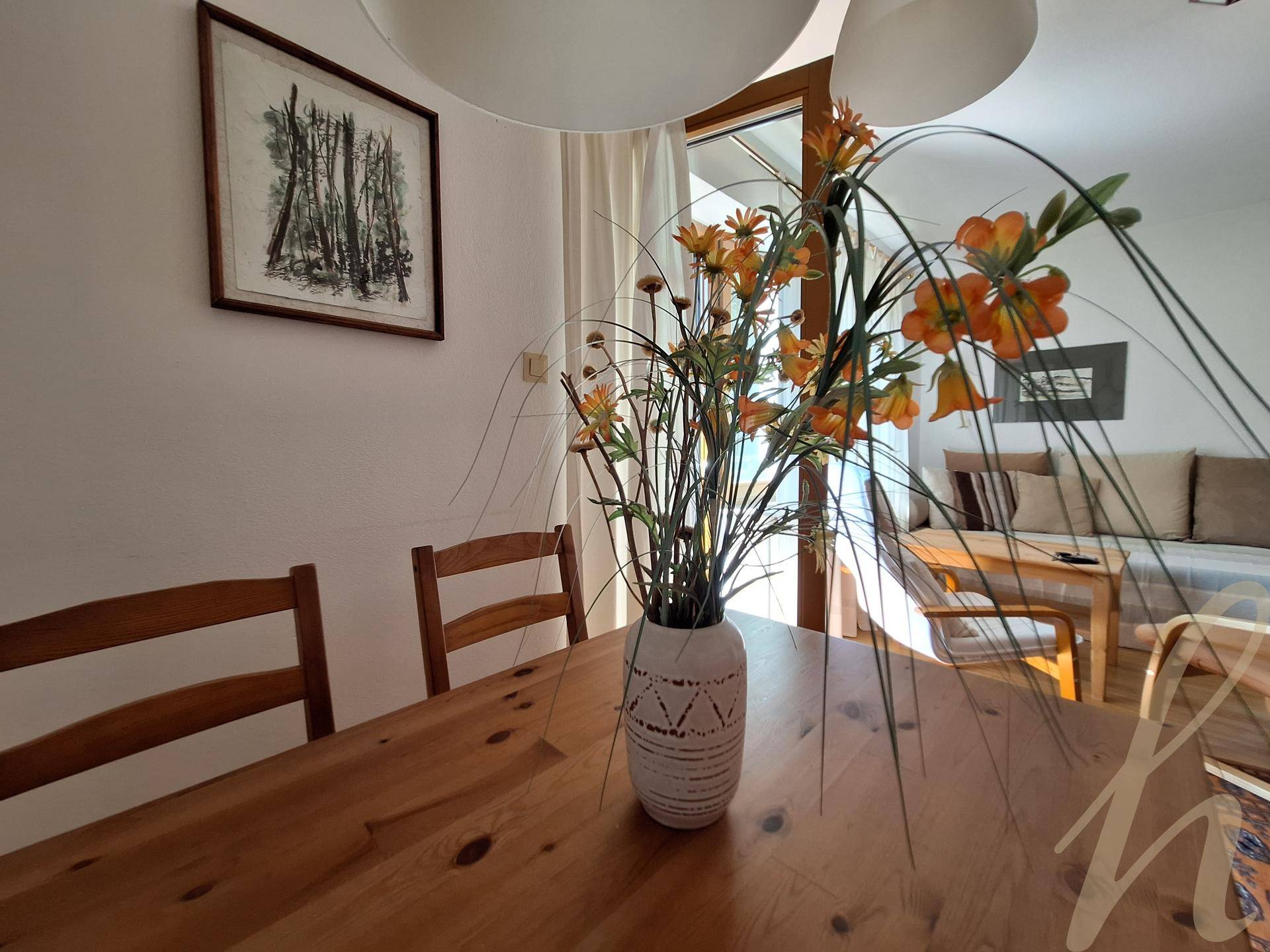 Gemütlicher Essbereich mit Holztisch, Stühlen und einem Blumenarrangement, angrenzend an den Wohnbereich.