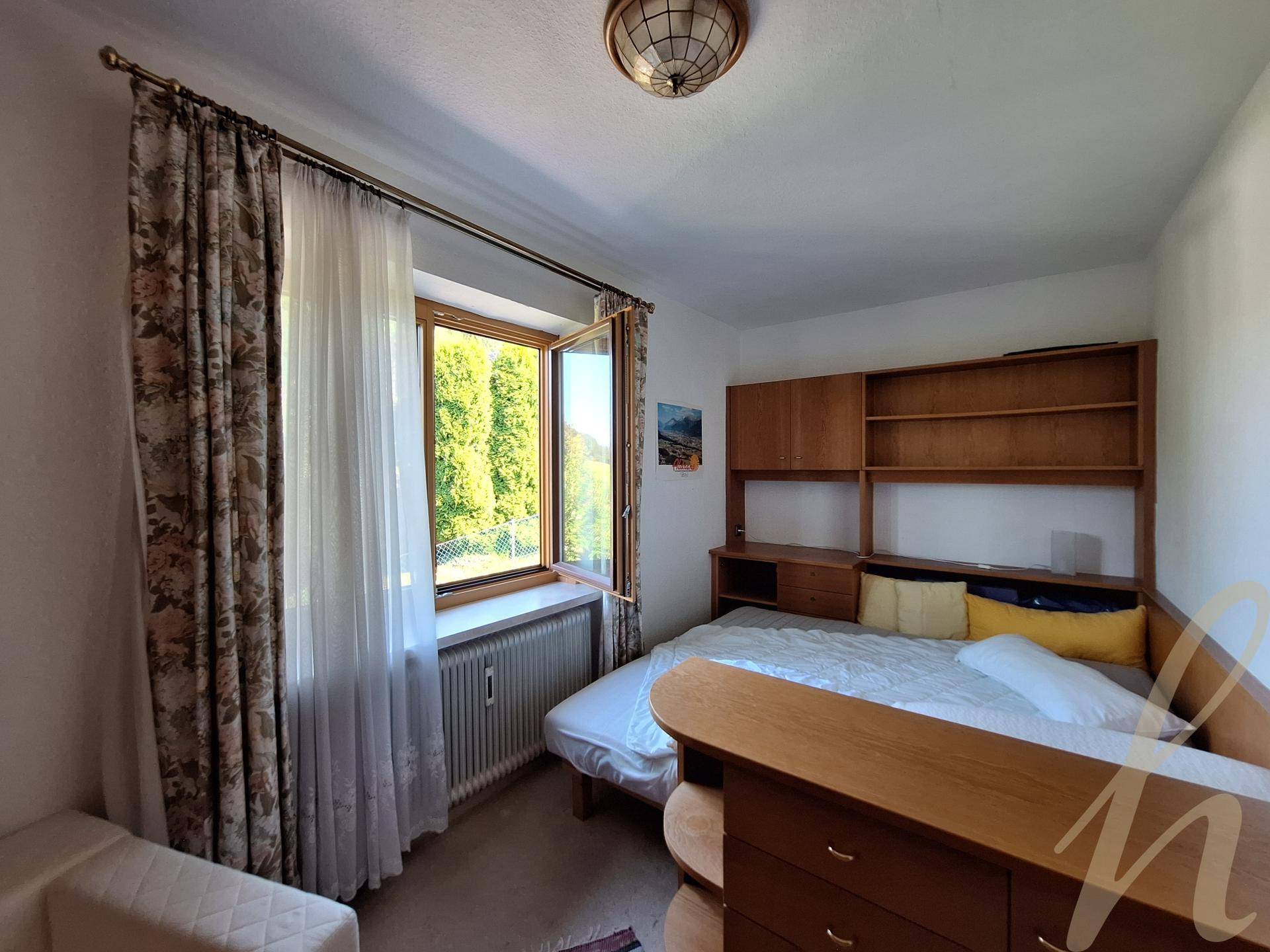 Gemütliches Schlafzimmer mit Holzbett, Einbauregalen und Fenster mit Blick ins Grüne.