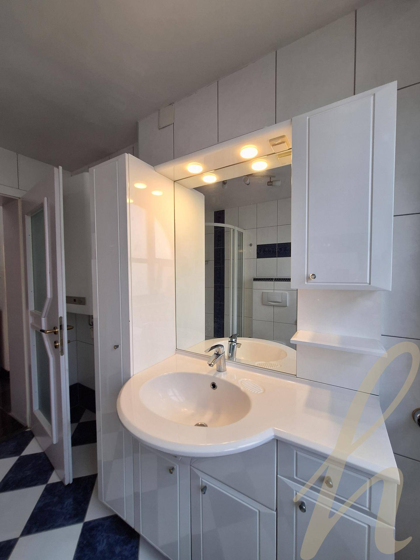 Badezimmer mit modernem Waschtisch, Spiegelschrank und weißen Fliesen, die eine helle Atmosphäre schaffen.