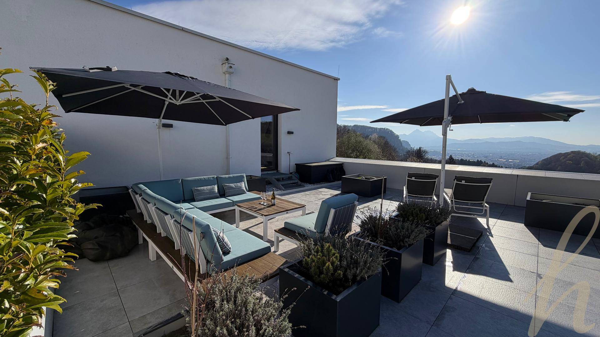 Sonnige Dachterrasse mit stilvollen Outdoor-Möbeln und weitem Blick über die Landschaft und Berge.
