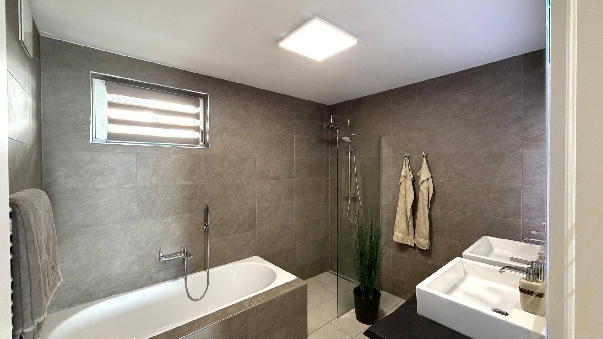 Modernes Badezimmer mit Badewanne, Dusche und Doppelwaschbecken in neutralen Farbtönen.