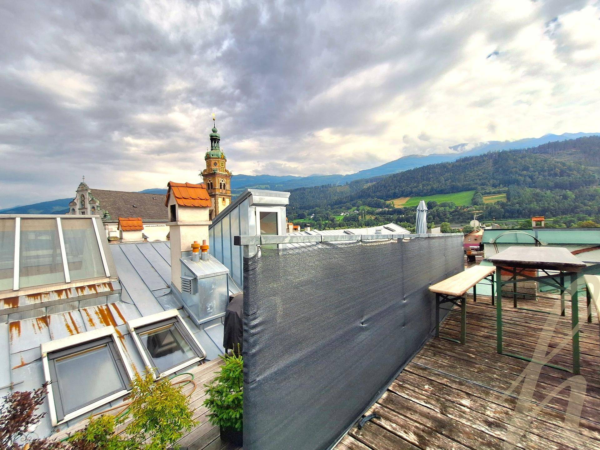 Geräumige Dachterrasse mit Holzboden, Sitzgelegenheiten und weitem Blick über die Stadt und die Berge.