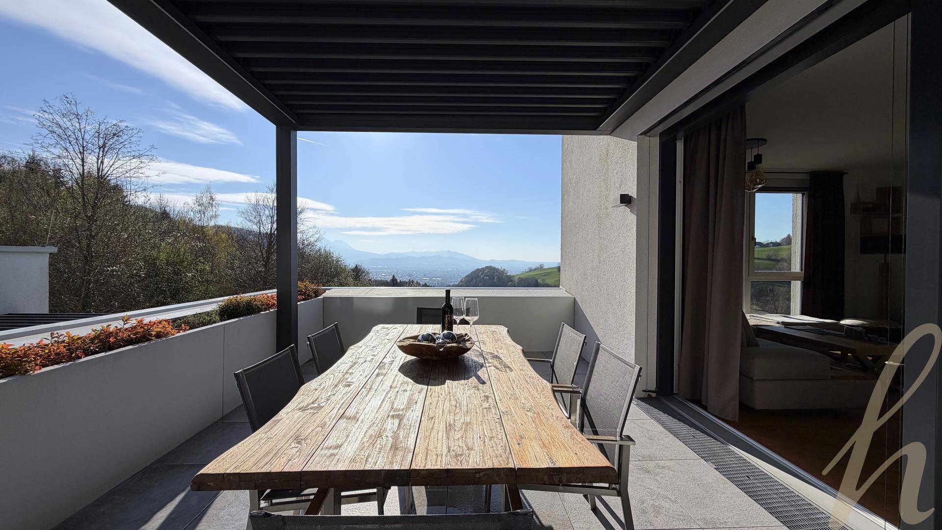 Überdachte Terrasse mit großem Holztisch und Stühlen, bietet einen weiten Blick auf die Landschaft.