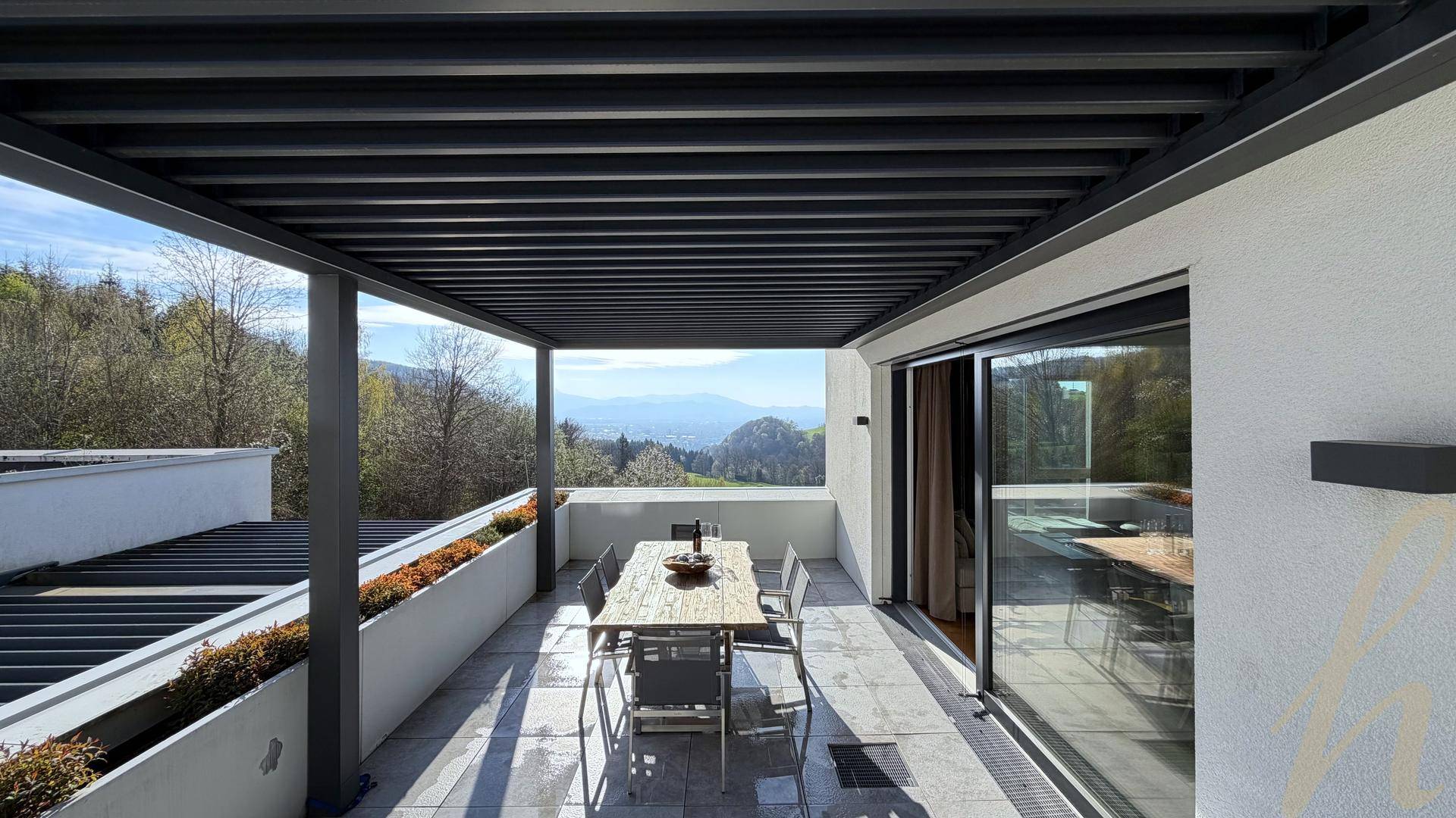 Geräumige, überdachte Terrasse mit Essbereich und Panoramablick auf die grüne Umgebung und Berge.