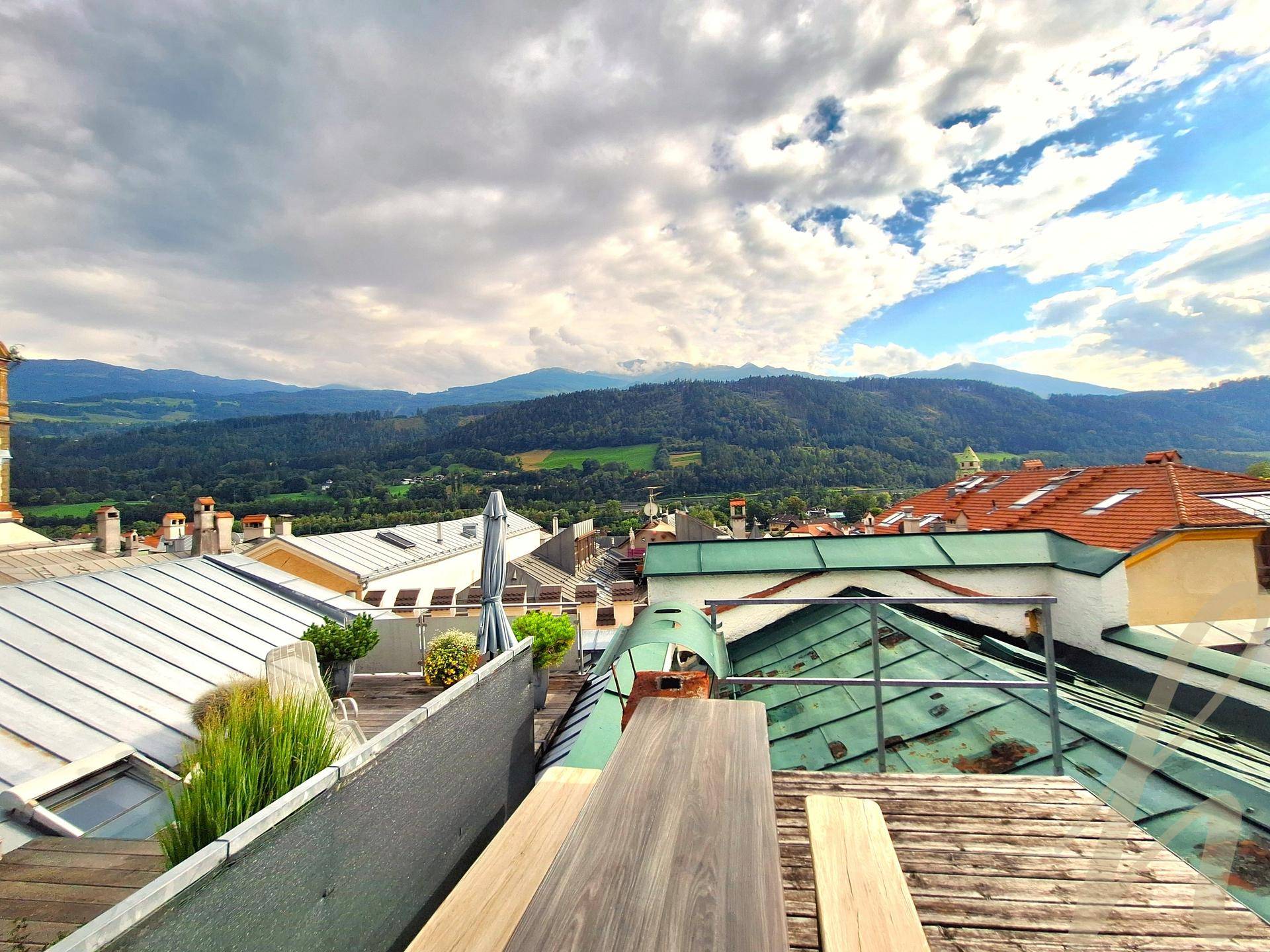 Panoramablick von der Dachterrasse mit Holzboden, Sitzbereich und einer beeindruckenden Bergkulisse.