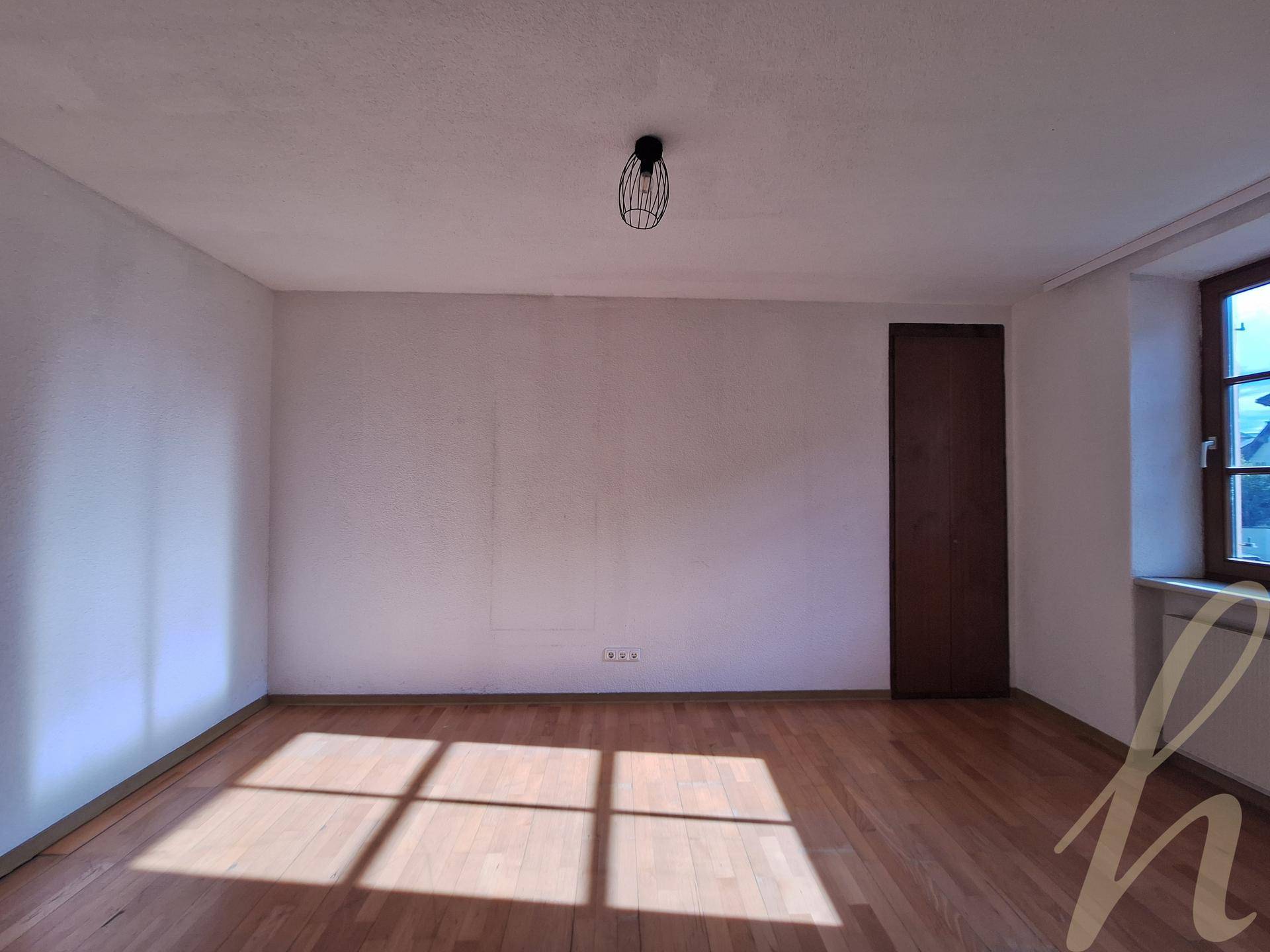 Leeres Zimmer mit Holzboden, einem Fenster und viel natürlichem Lichteinfall, bereit zur individuellen Gestaltung.