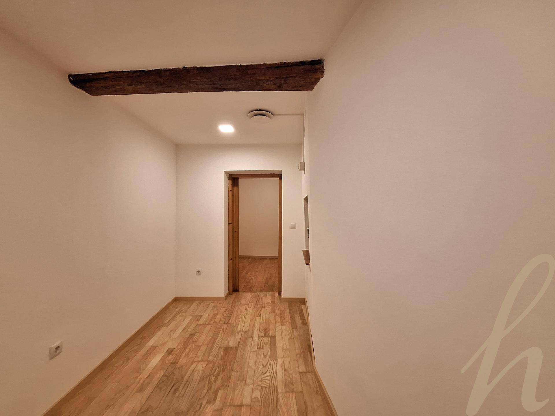 Langer Flur mit hellem Holzboden, weißen Wänden und einem rustikalen Holzbalken an der Decke.