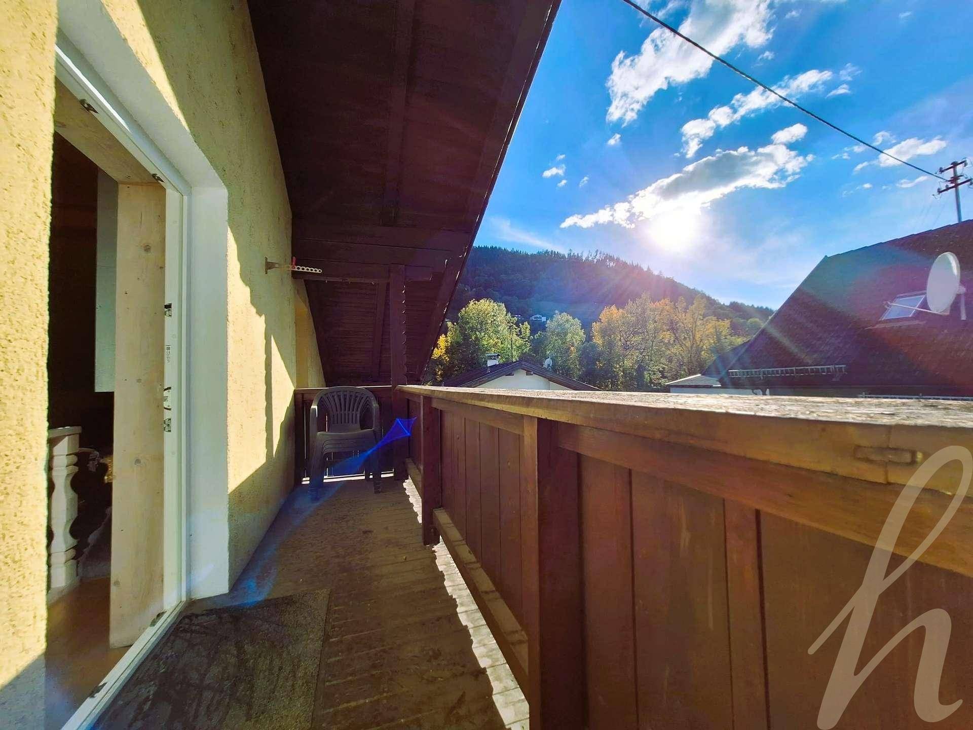 Sonniger Balkon mit Holzgeländer und Blick auf die grüne Hügellandschaft.
