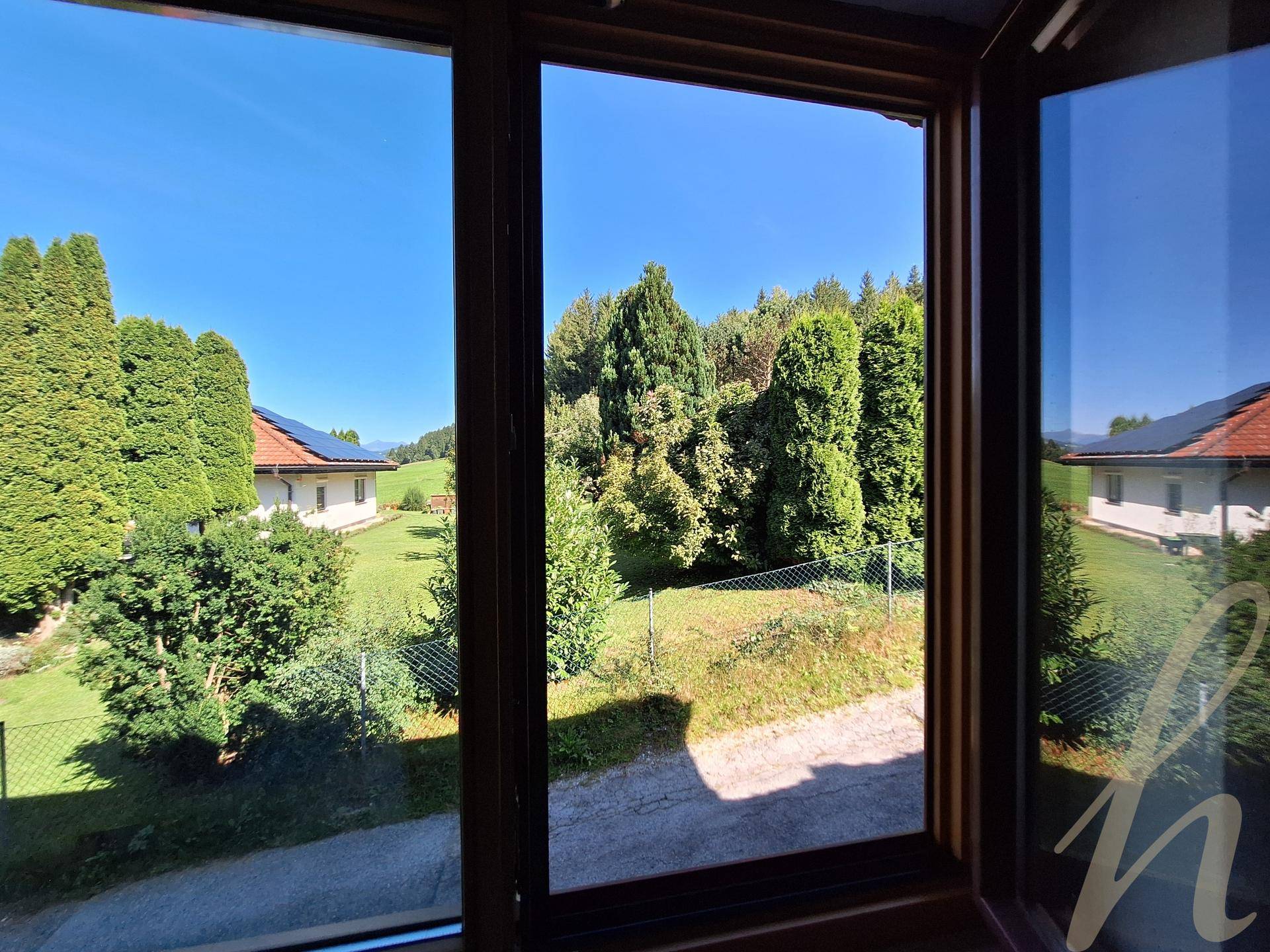 Blick aus einem Fenster auf einen grünen Garten mit Bäumen und weiteren Häusern in der Ferne.