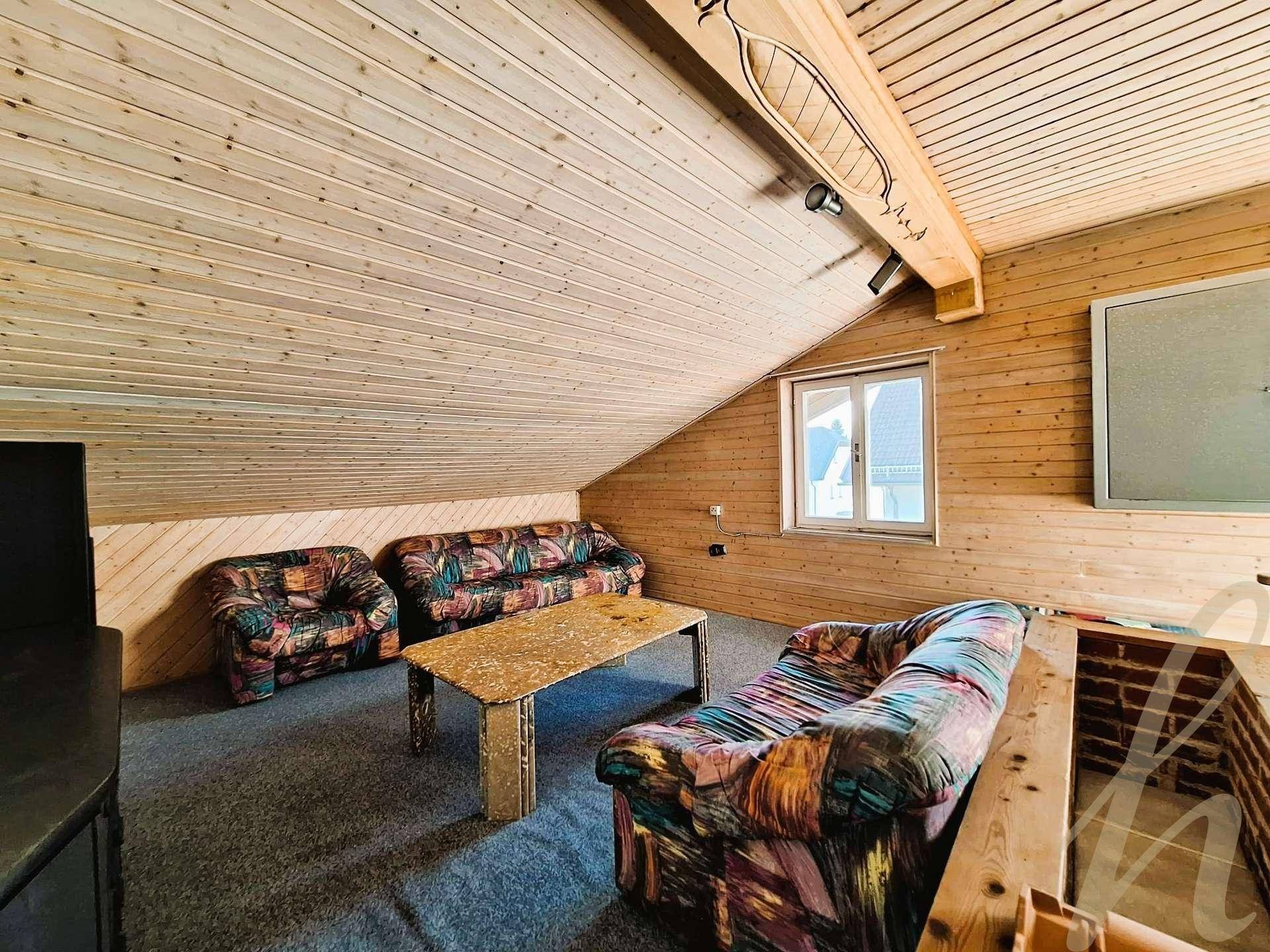 Gemütlicher Dachbodenraum mit Holzverkleidung, Teppichboden und Sitzgelegenheiten.