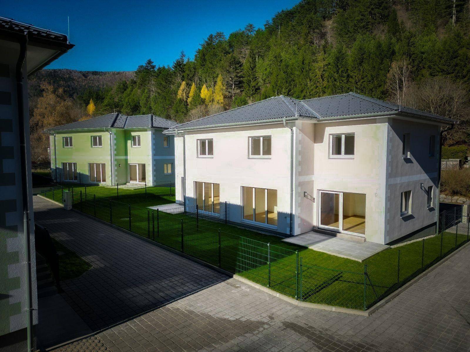 Zwei moderne Häuser mit hellen Fassaden, großen Fenstern und frisch angelegten Gärten.