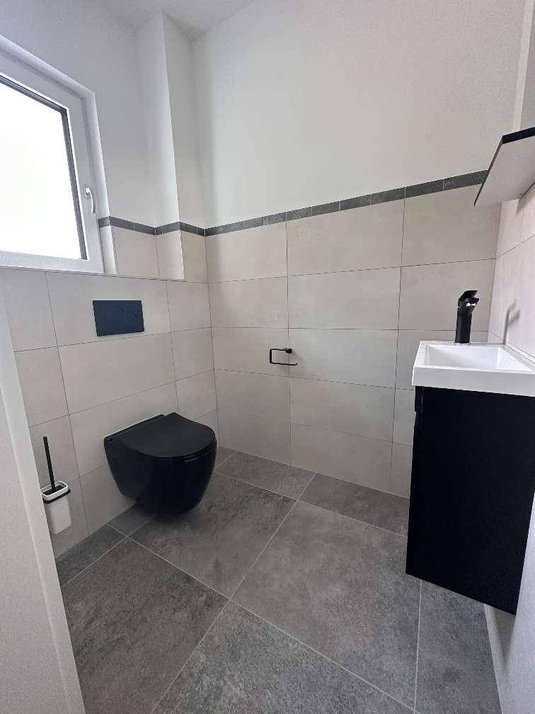 Modernes Gäste-WC mit dunklen Fliesen, wandhängendem WC und Fenster.