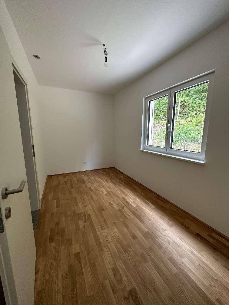 Schlafzimmer mit Holzboden und großem Fenster mit Blick ins Grüne.