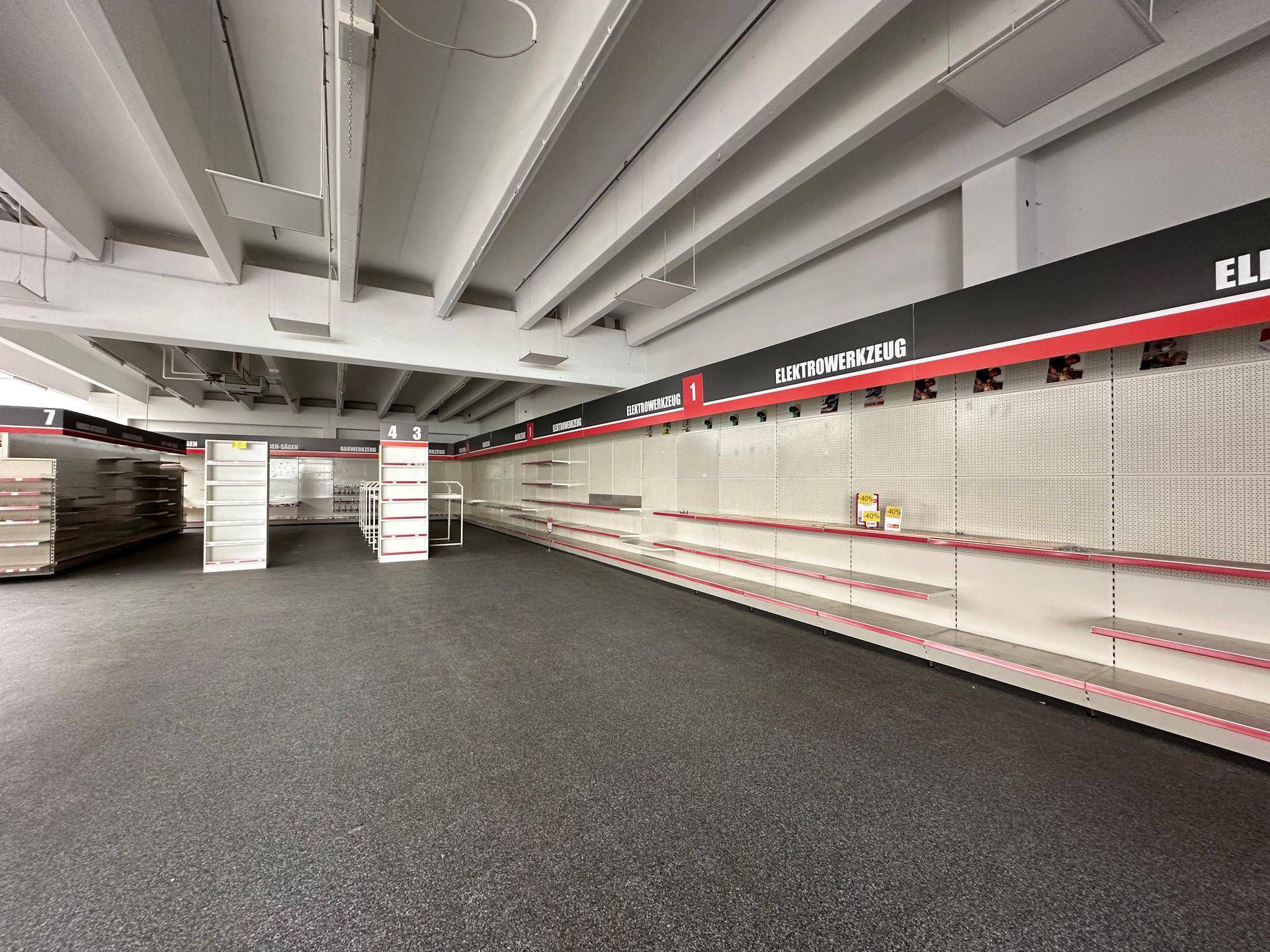 Weitläufiger, leerer Verkaufsraum mit langen Regalreihen und einem dunklen, strapazierfähigen Bodenbelag.