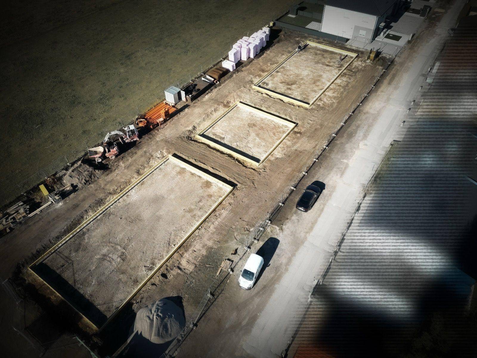 Luftaufnahme einer Baustelle mit mehreren vorbereiteten Fundamenten für Reihenhäuser.