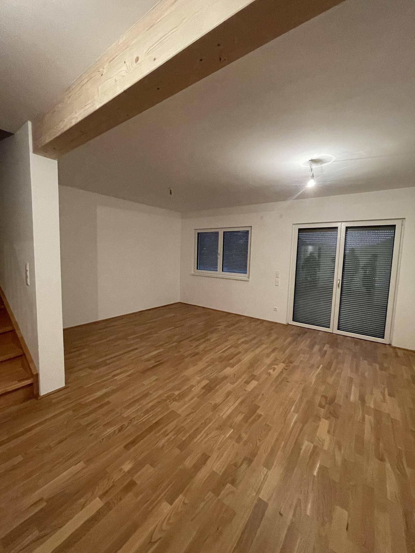 Wohnzimmer mit Holzboden und Rollläden an der Terrassentür, abends beleuchtet.