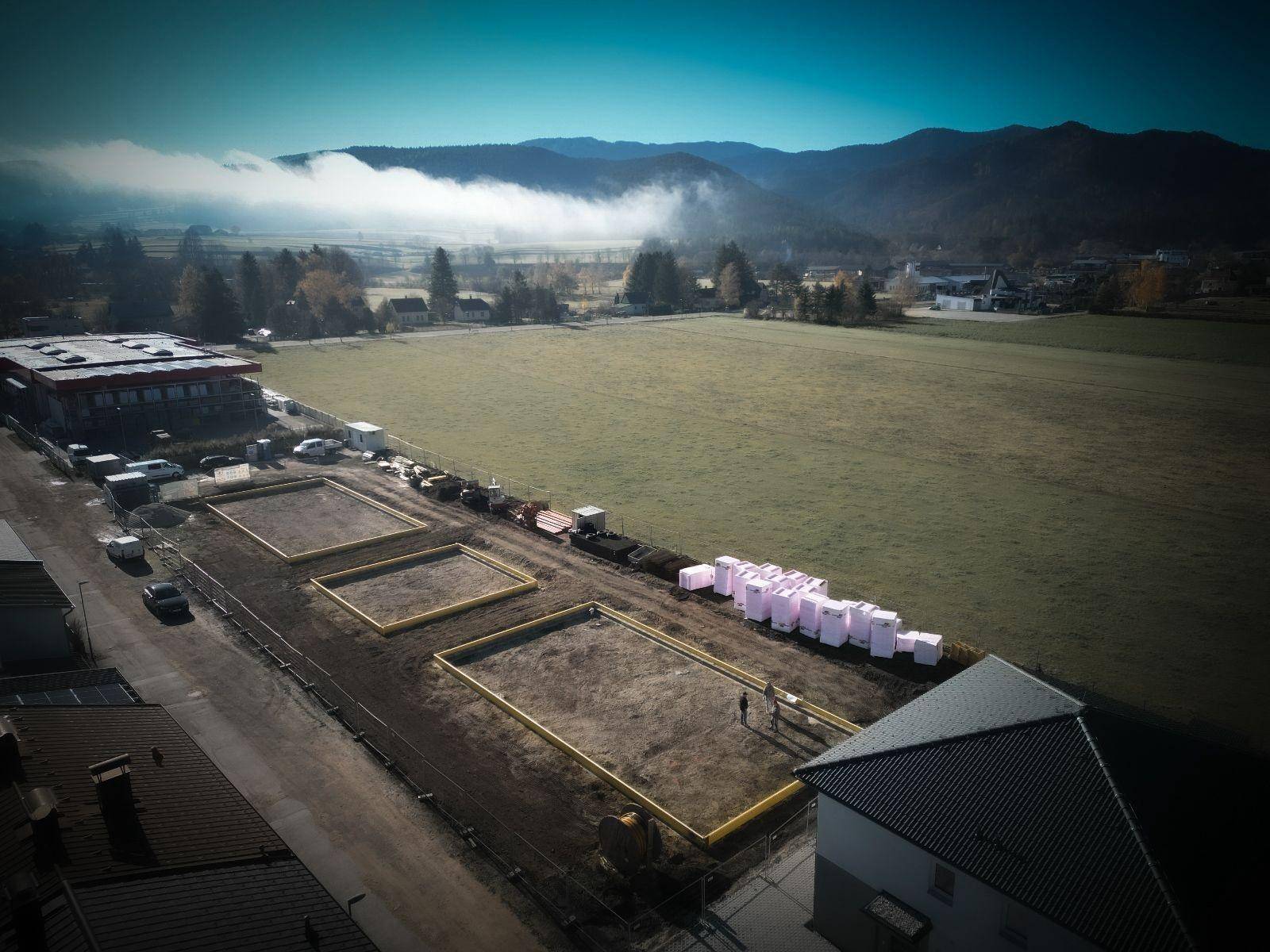 Luftaufnahme einer Baustelle mit Fundamenten und malerischem Bergblick im Hintergrund.