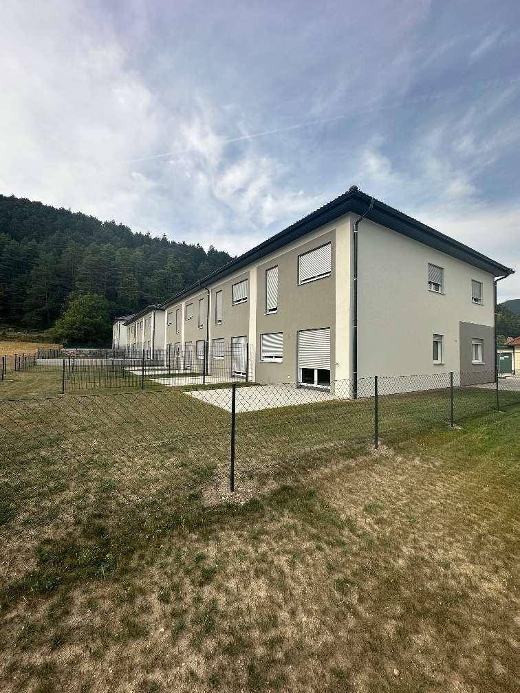 Rückansicht der Reihenhäuser mit kleinen Gärten und Blick auf bewaldete Hügel.