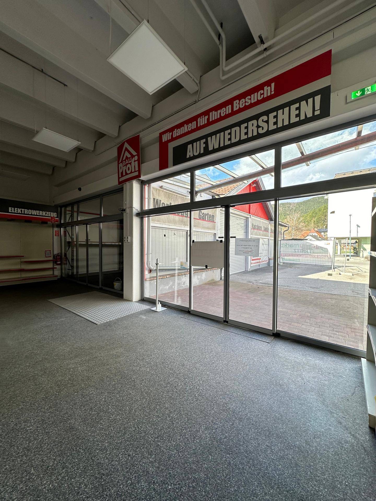 Heller Verkaufsraum mit großen Fensterfronten und Blick nach draußen, ausgestattet mit grauem Bodenbelag.