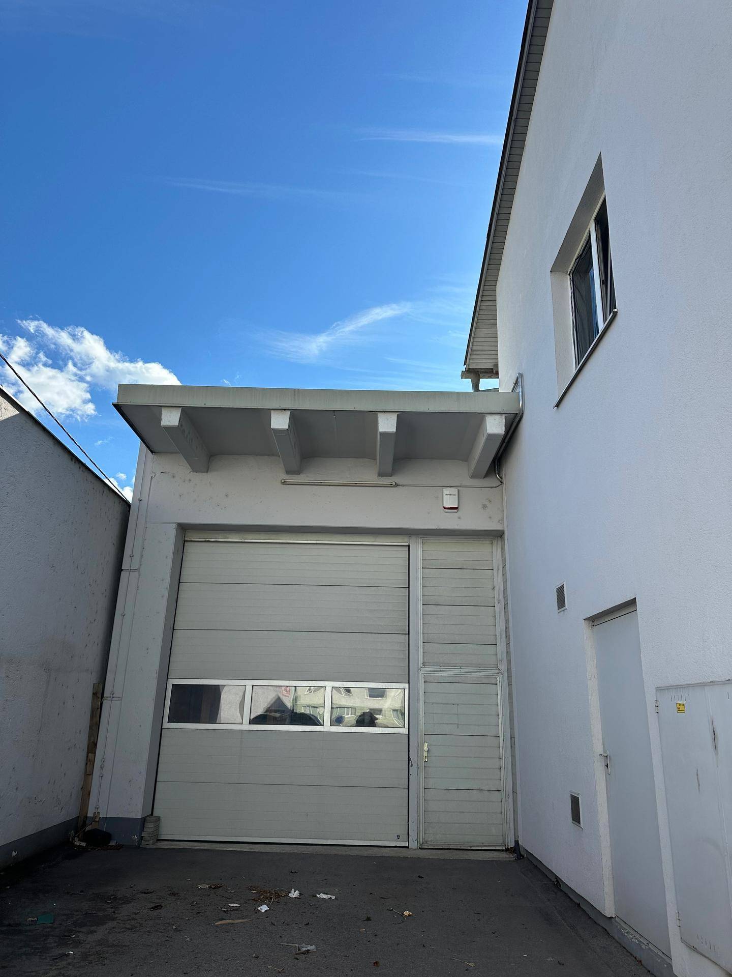 Rückseite des Gebäudes mit einem großen Garagentor und einer schlichten weißen Fassade unter blauem Himmel.