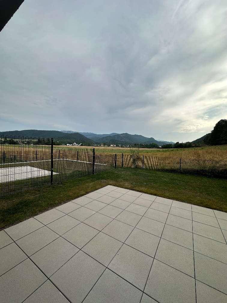 Gepflasterte Terrasse mit Rasenfläche und weitem Blick auf die Landschaft.