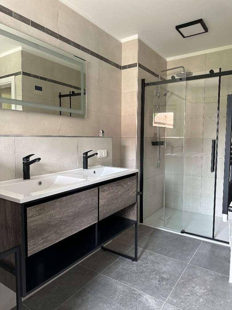 Modernes Badezimmer mit Doppelwaschbecken, großer Dusche und dunklen Armaturen.
