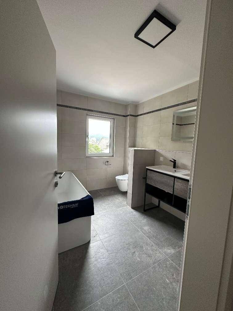 Modernes Badezimmer mit Badewanne, Fenster und dunklen Bodenfliesen.