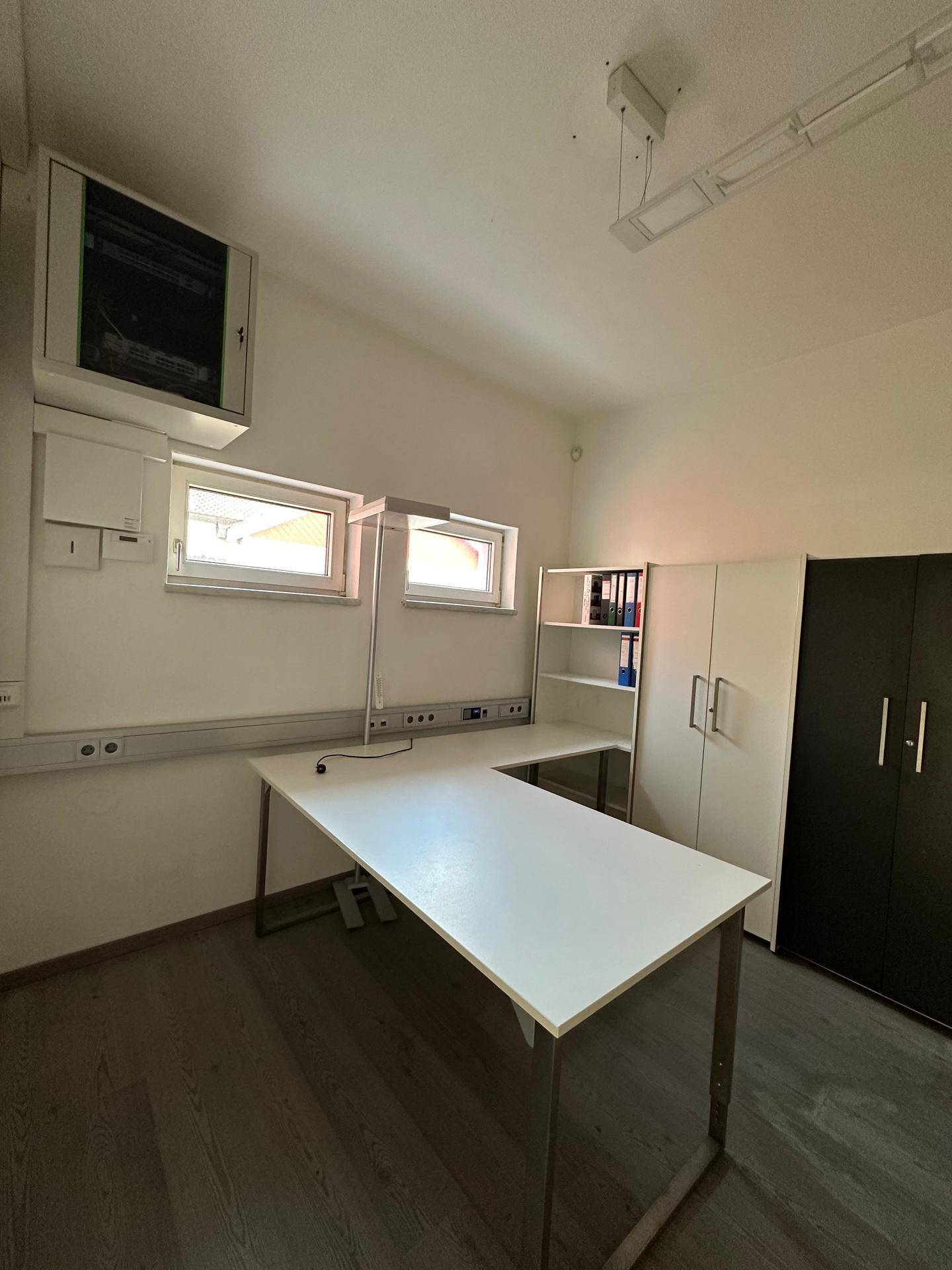 Helles Büro mit Schreibtisch, Schränken und zwei Fenstern, ausgestattet mit modernem Bodenbelag.