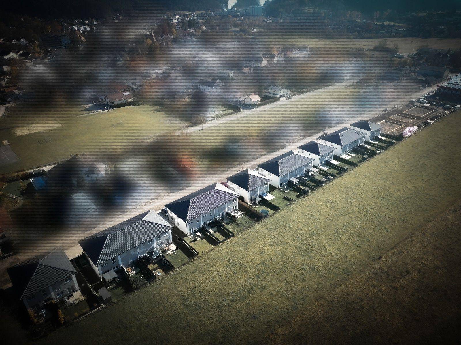 Weitläufige Luftaufnahme einer Siedlung von Reihenhäusern neben einem Feld.