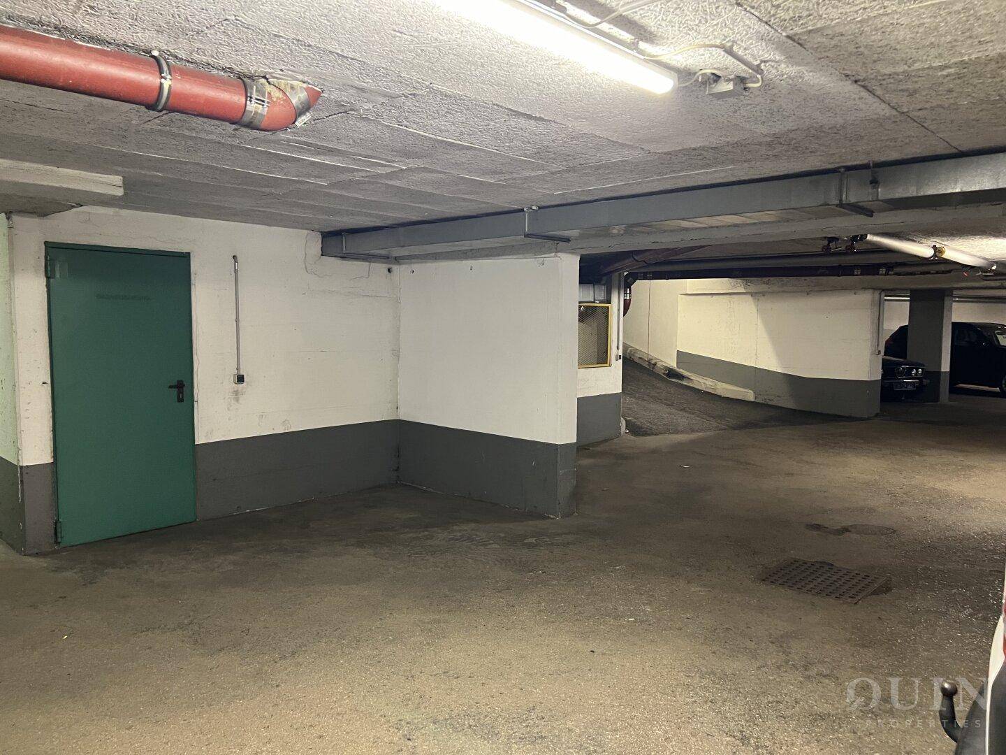 Geräumige Tiefgarage mit grünem Zugangstor und Zufahrt im Hintergrund.