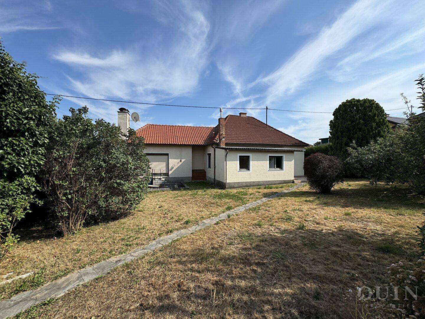 Rückansicht des Hauses mit großem Gartenbereich unter blauem Himmel.