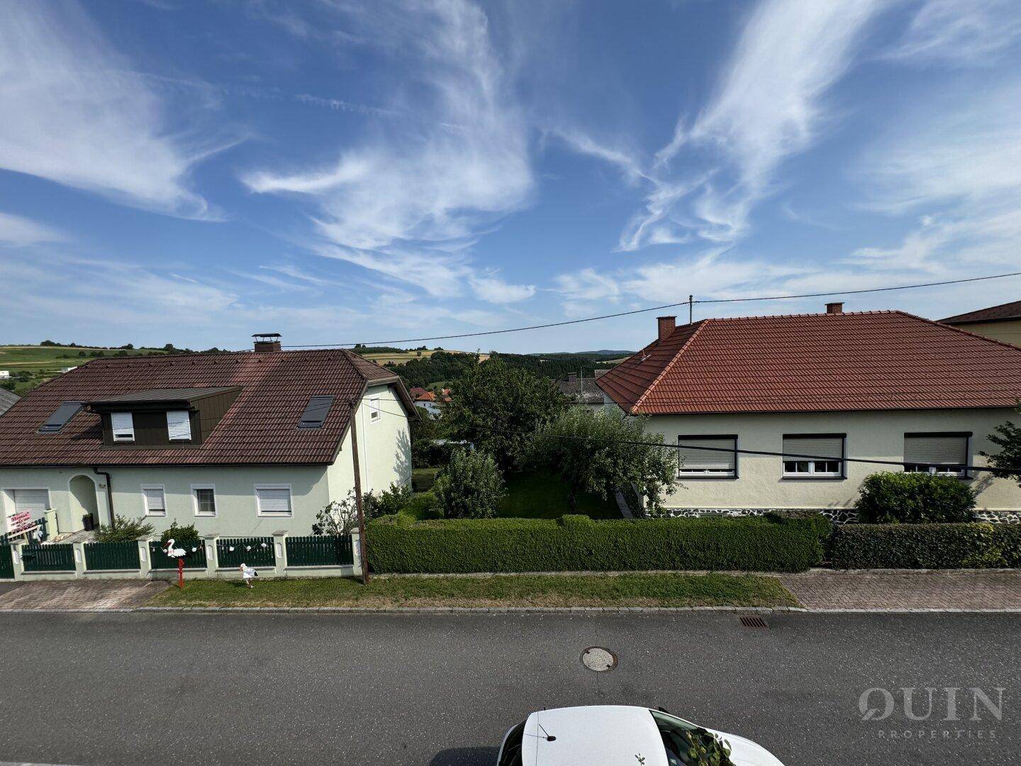 Blick auf die Nachbarschaft mit weiteren Häusern und grünen Hügeln im Hintergrund.