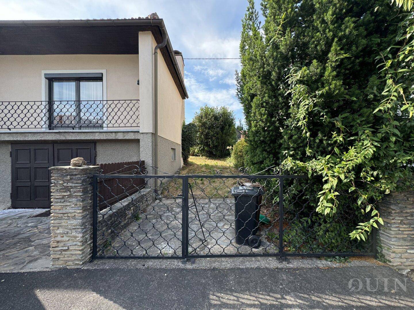 Seitenansicht des Hauses mit Einfahrt zur Garage und hohen Bäumen.