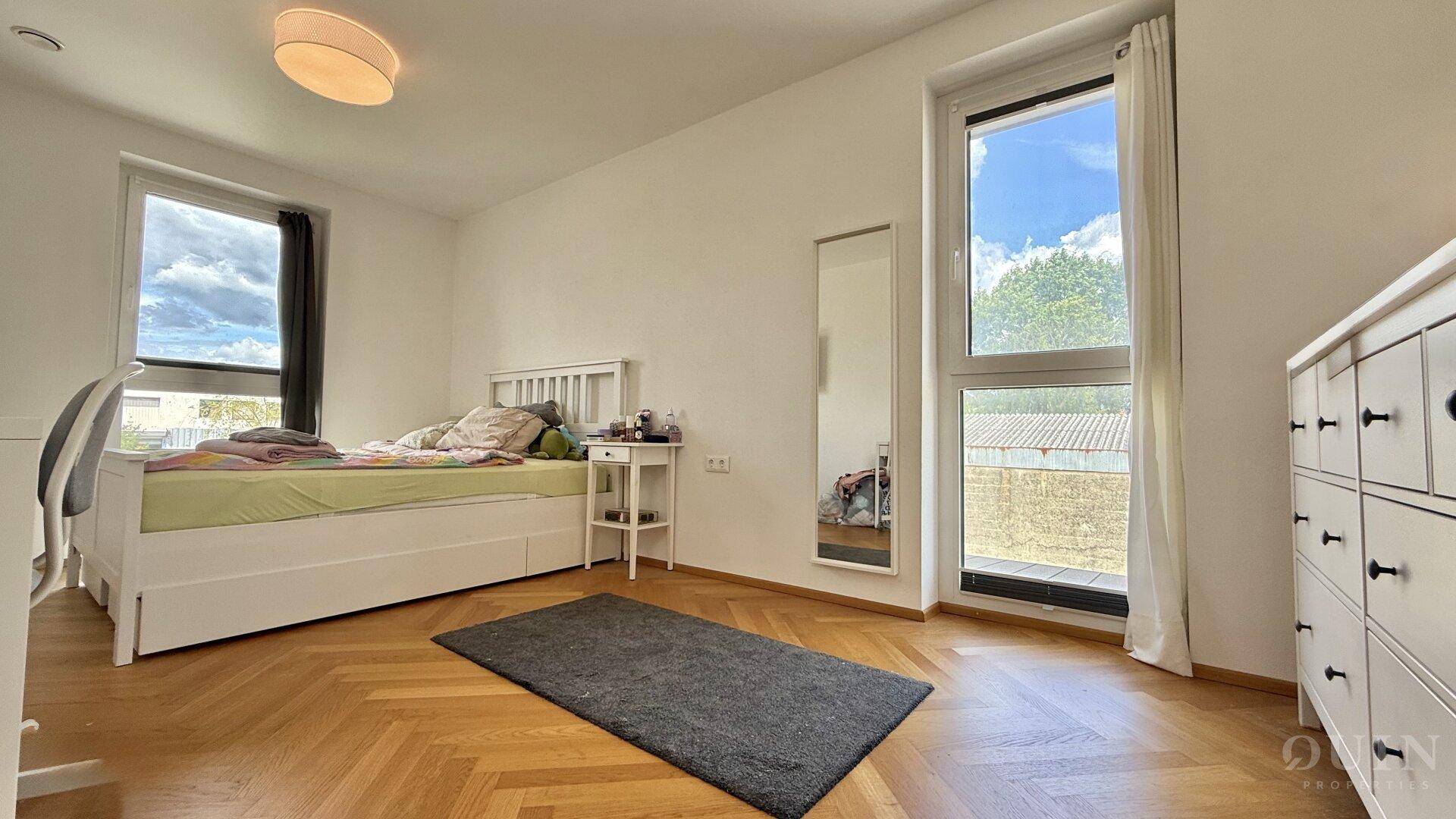 Helles Schlafzimmer mit Parkettboden, großem Fenster und Blick ins Grüne.