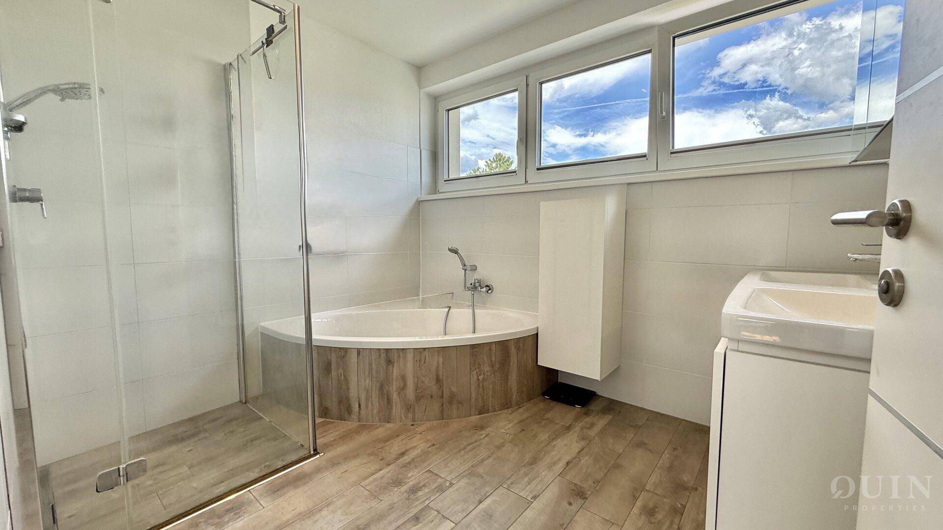 Modernes Badezimmer mit Eckbadewanne, Dusche, Waschbecken und Fenster.