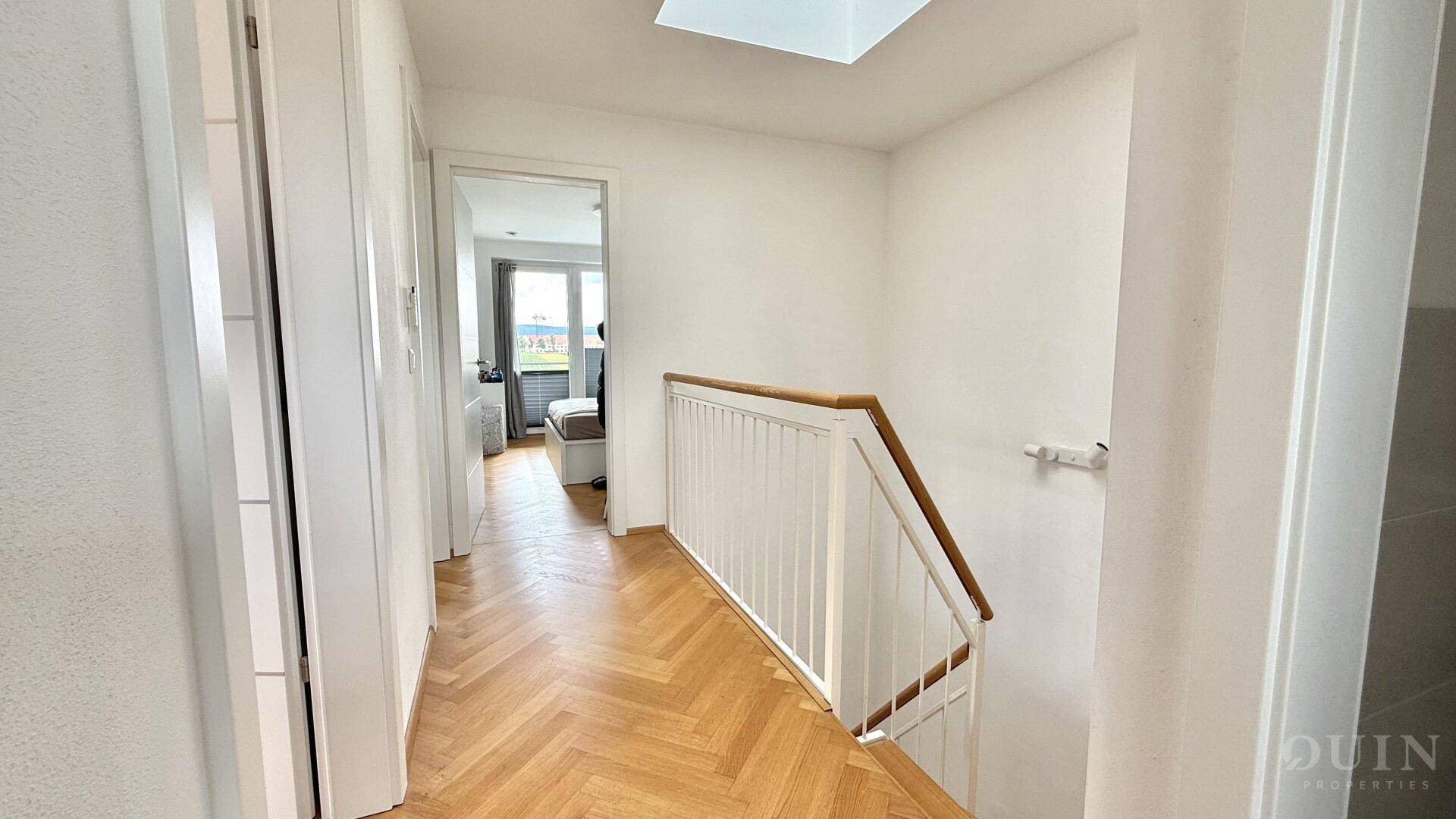 Heller Flur im Obergeschoss mit Parkettboden, Treppengeländer und Blick in ein Schlafzimmer.